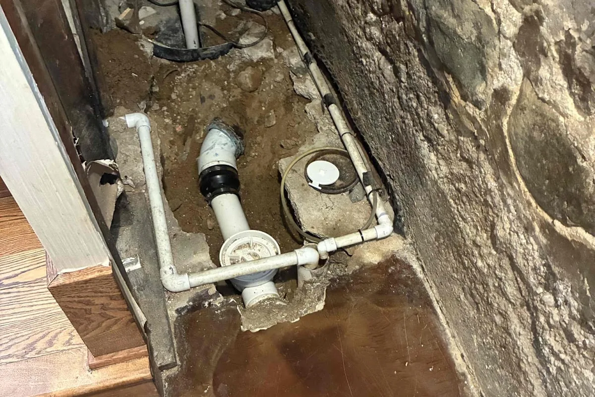 New PVC sewer line with two cleanouts installed at a basement foundation wall
