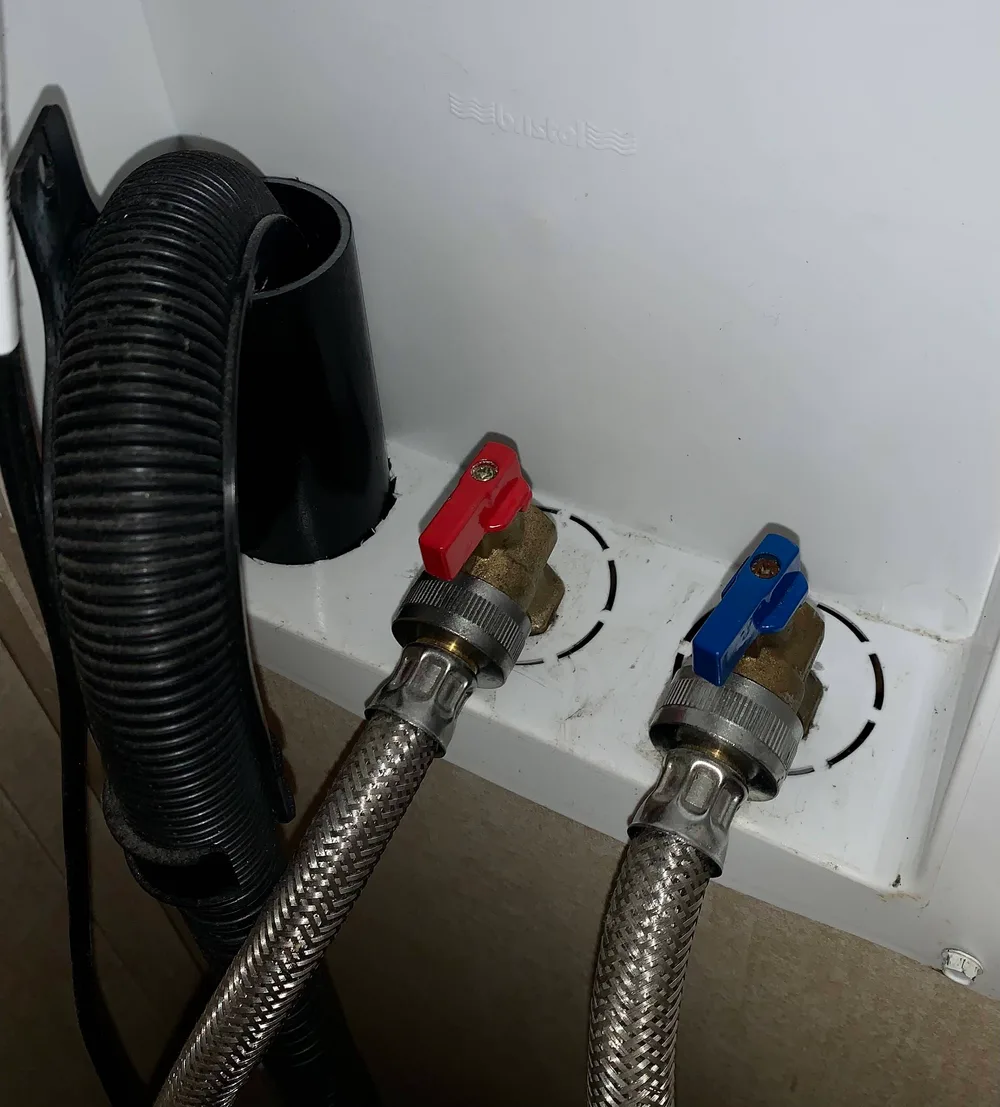 Hot and cold shut-off valves with red and blue levers behind a washing machine