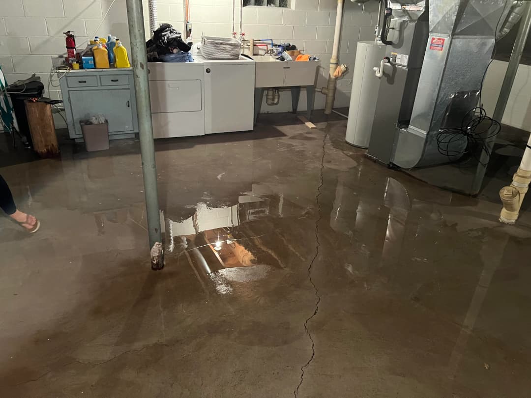 Basement sewer backup with sewage water pooling on the floor after heavy rain in West Michigan.