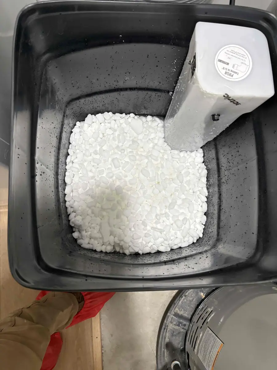 Top of a brine tank filled with white salt pellets next to a new softener