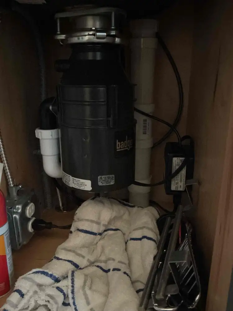 An older InSinkErator Badger disposal unit under a sink with towels placed below to catch a slow leak