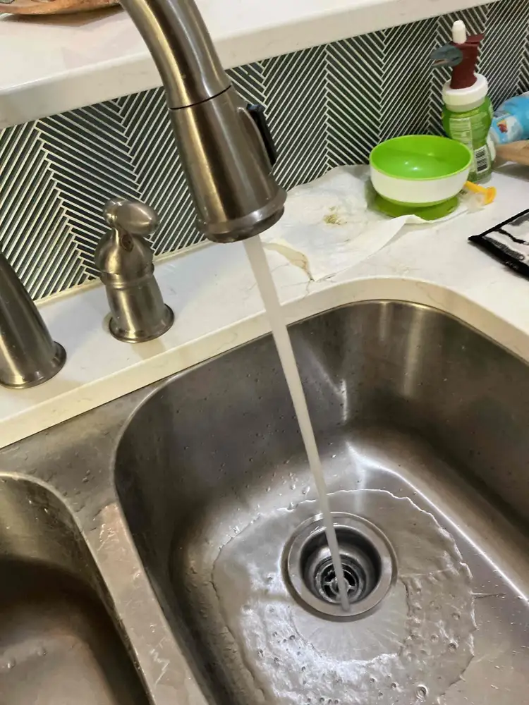 Cold water running into a stainless steel kitchen sink with the garbage disposal drain visible at the bottom of the basin