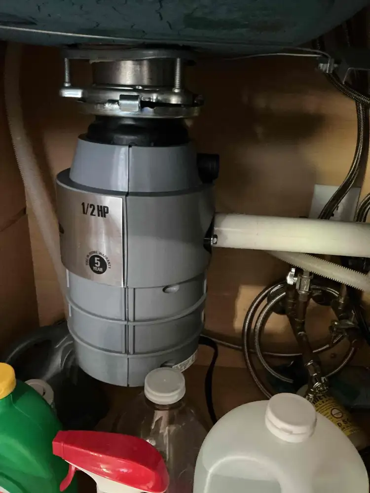 A half horsepower garbage disposal unit mounted under a kitchen sink showing the mounting ring and drain outlet connection