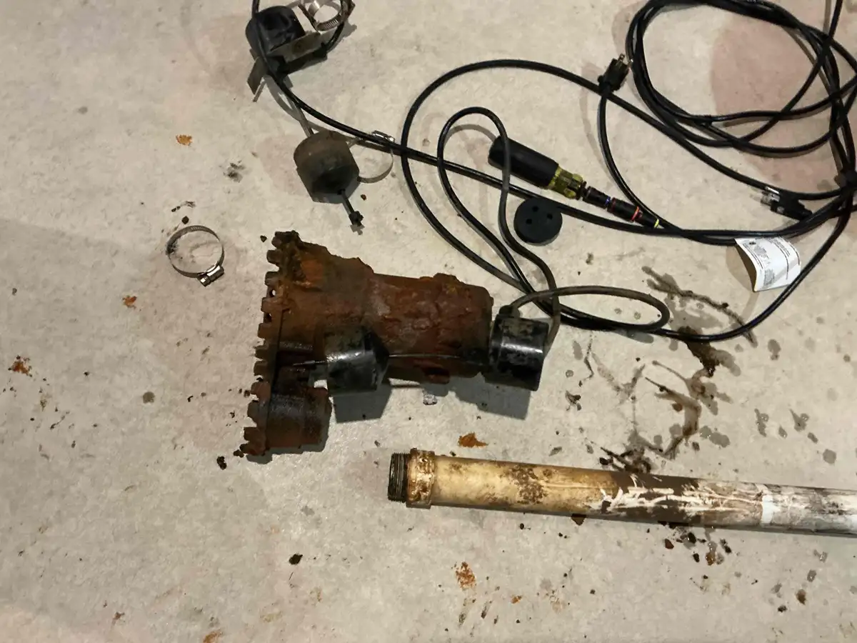 Failed sump pump pulled from the pit, rusted through and lying beside its old discharge pipe