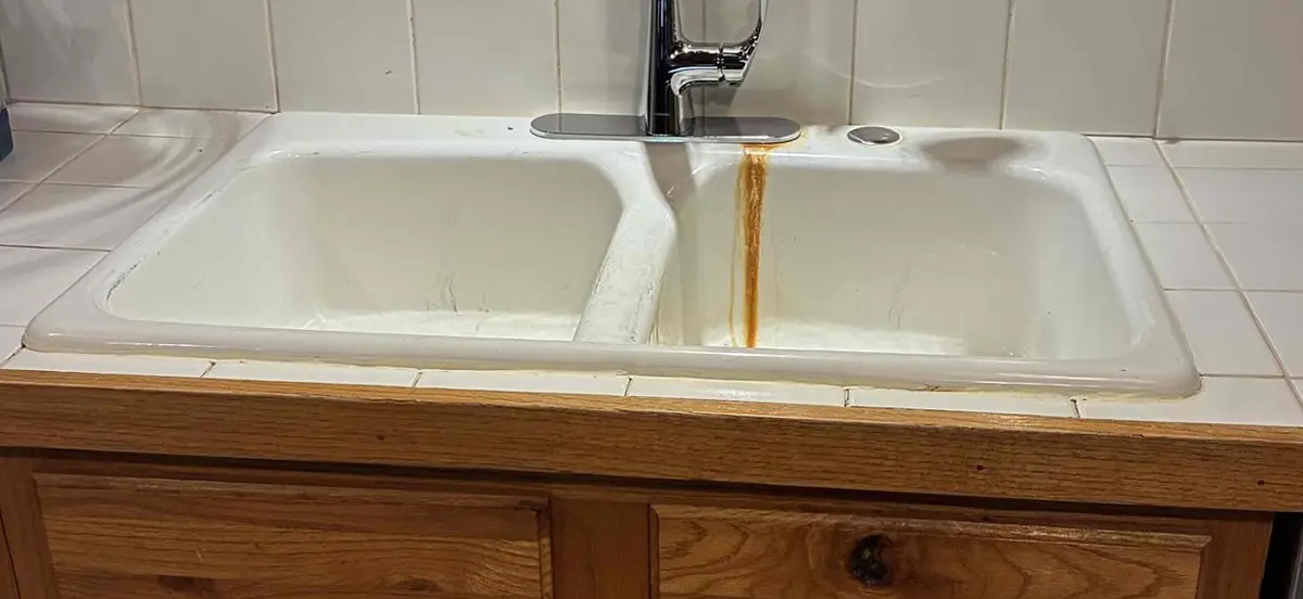 Orange iron stain running down a white kitchen sink below the faucet