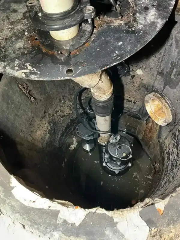 Old corroded sump pump inside a rusted sump crock with heavy staining around the rim