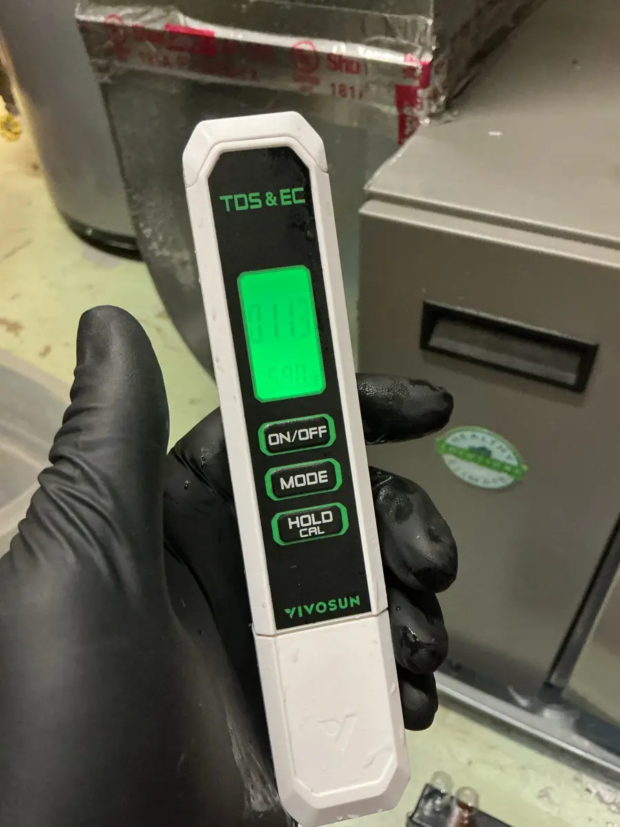 Technician holding a TDS and EC meter reading a water sample before a softener install