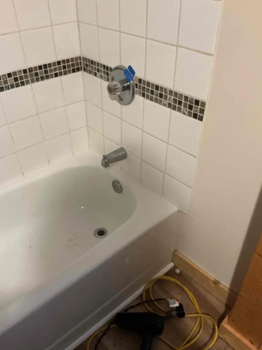 Bathtub with the faucet opened and a hair dryer on the floor below while a frozen supply pipe thaws