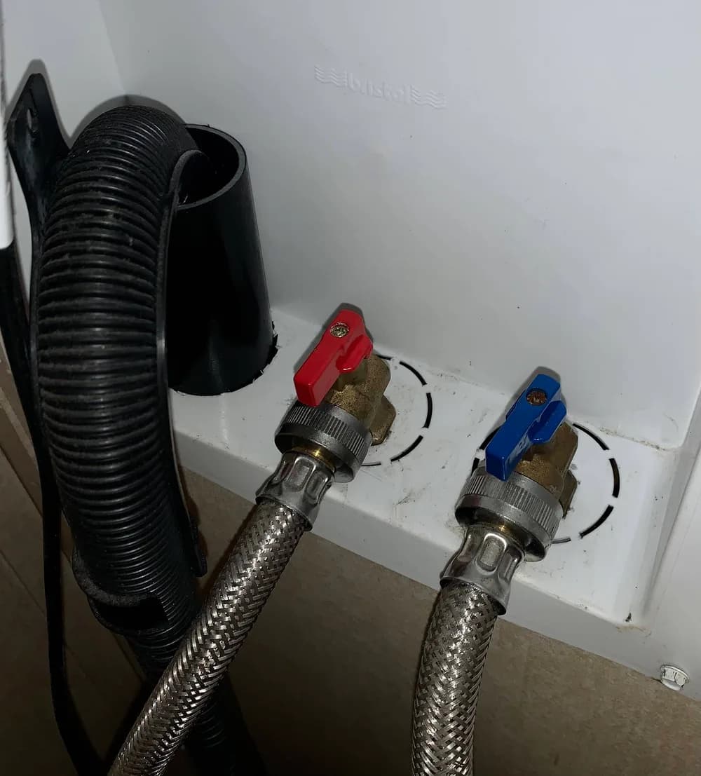 Hot and cold shut-off valves with red and blue levers behind a washing machine