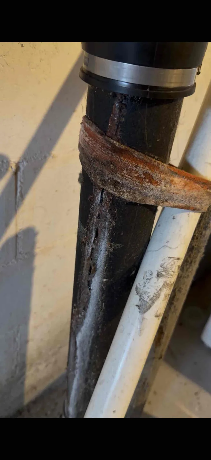 Close up of a rusted, flaking cast iron drain stack with a crust of corrosion wrapped around the pipe