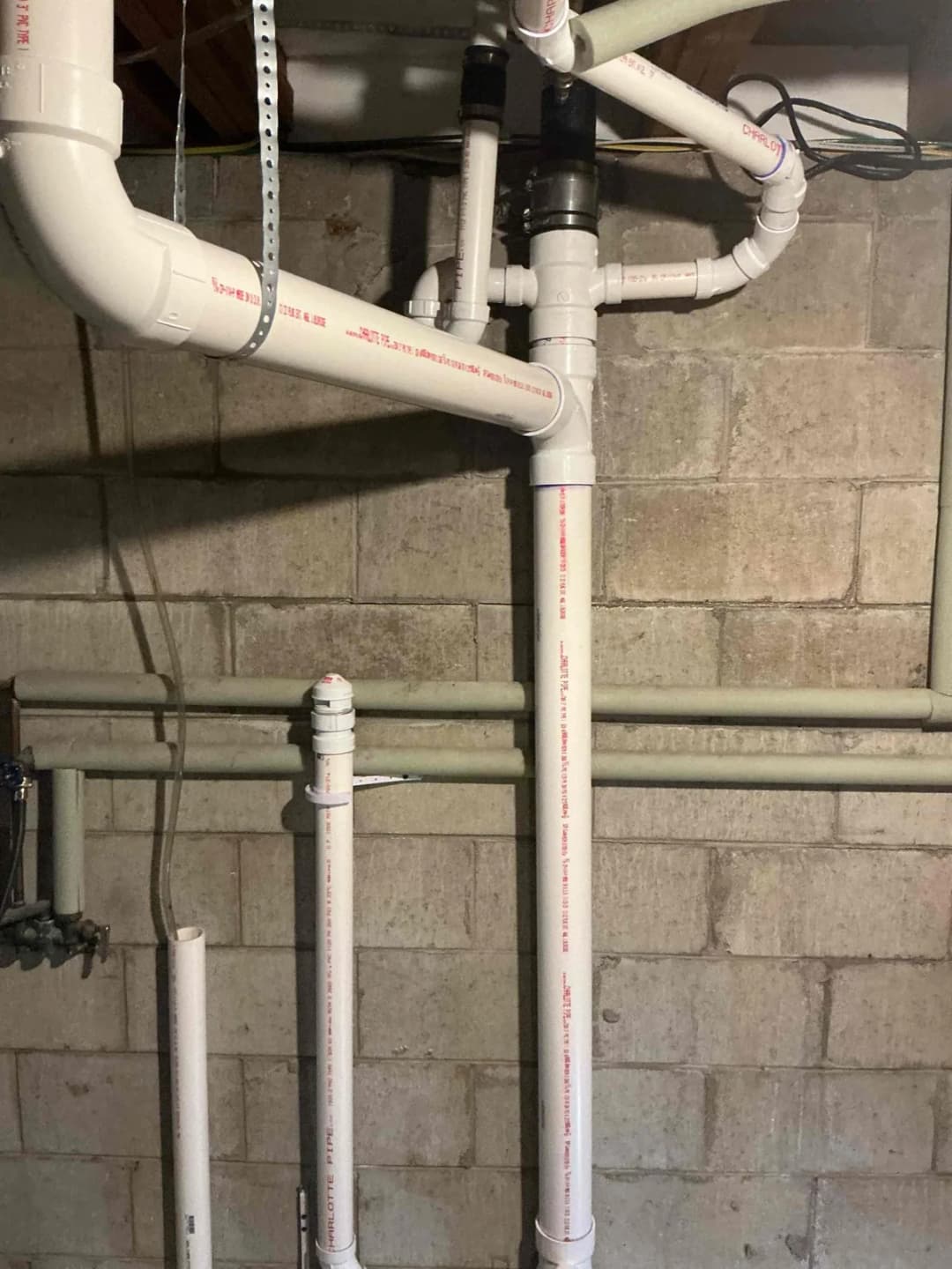 New white PVC main stack with branch connections and a cleanout installed against a basement block wall