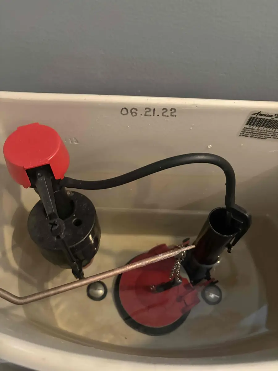 Inside of a toilet tank showing the manufacture date 06.21.22 molded into the porcelain back wall above a new red flapper and fill valve
