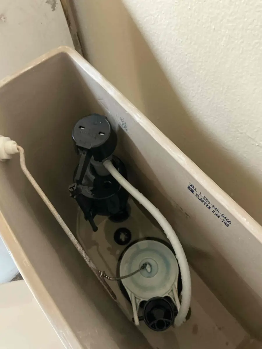 Inside of a toilet tank with the manufacturer help line and flapper part number 99-788 printed on the porcelain wall next to the fill valve and flapper