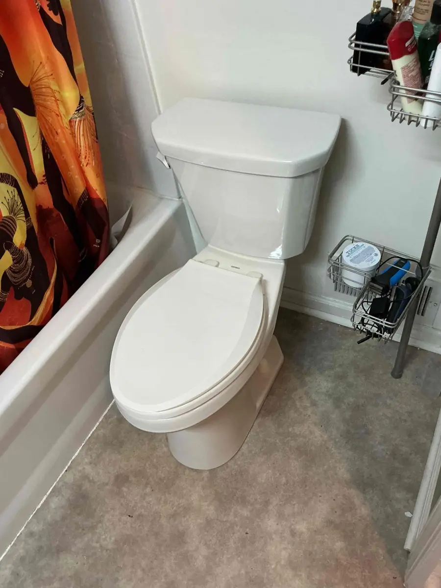 New white two piece toilet installed against a tiled tub surround with the floor cleaned up around the base