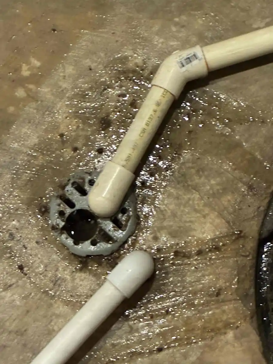 Wet basement floor around a floor drain with a white PVC drain pipe lying on the concrete