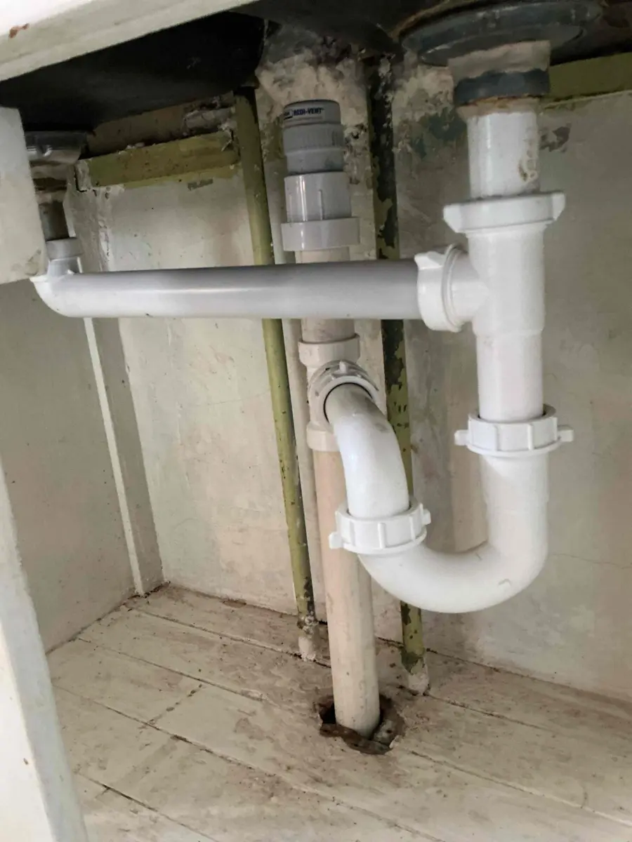 Bathroom sink drain trap under a vanity cabinet with white plastic pipes and joints
