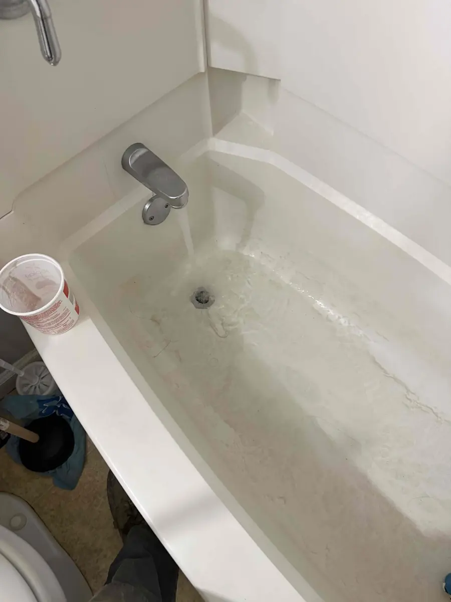 Bathtub with a few inches of gray standing water that will not drain