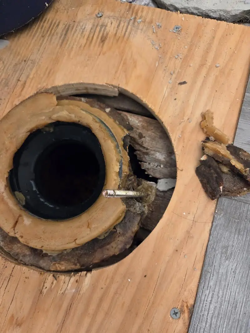 Broken toilet flange on an old drain pipe with rotted and soft subfloor around the opening
