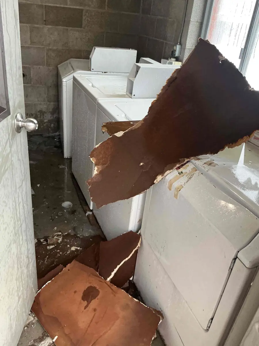 Laundry room with washers and a large piece of collapsed drywall ceiling hanging down after a burst pipe