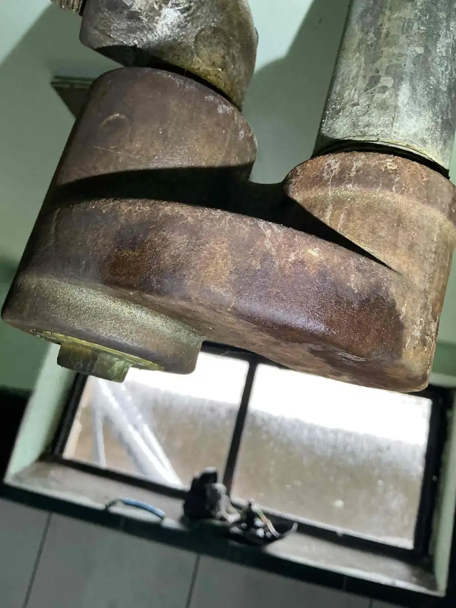 Corroded metal tub drain fitting under an older bathtub seen from the basement ceiling