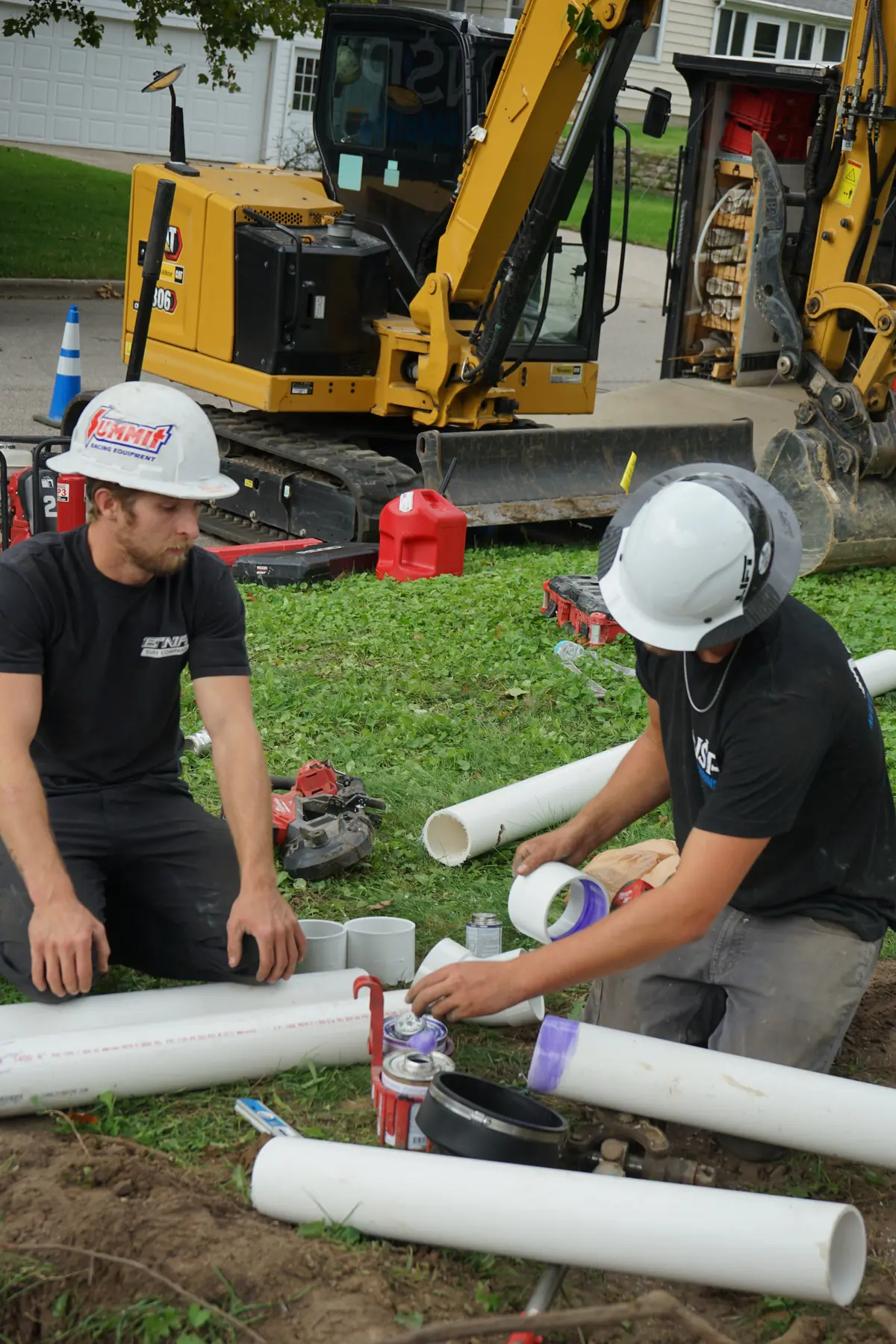 NSP Plumbing crew fitting new PVC sewer pipe beside a mini excavator during a sewer line replacement