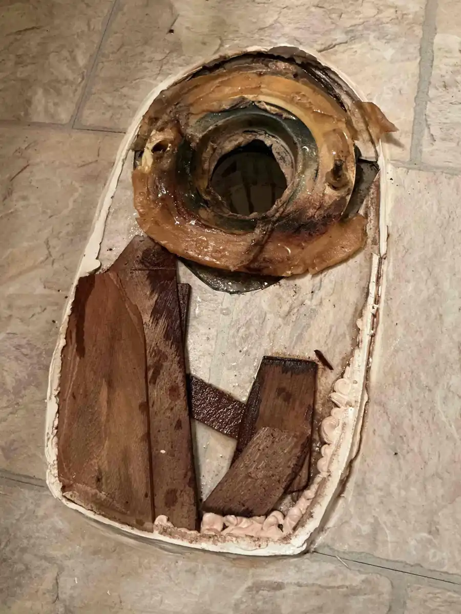 Toilet removed from a bathroom floor showing a failed wax seal and rotted wood subfloor around the drain opening