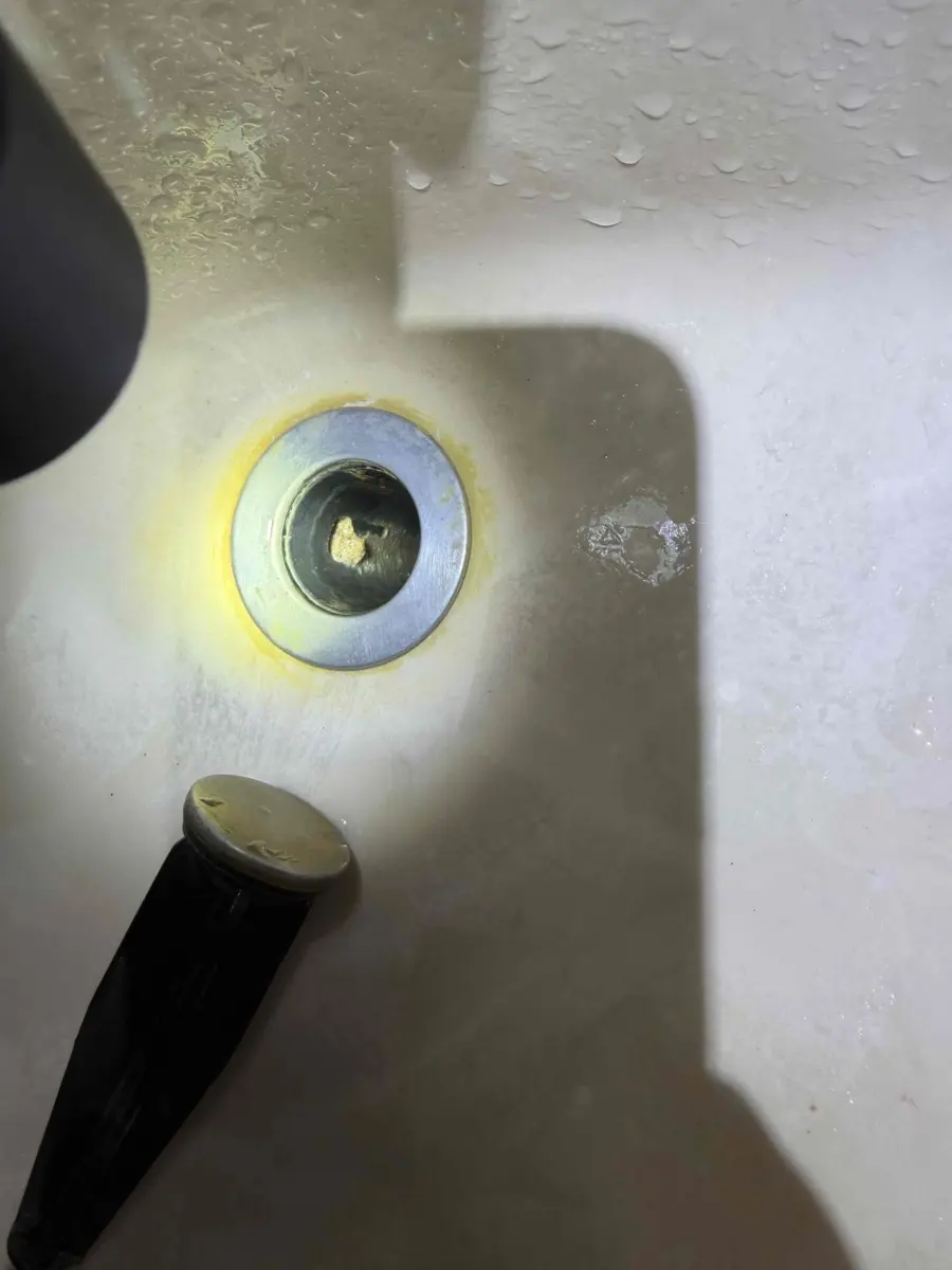 Flashlight shining into a bathroom sink drain opening around the stopper