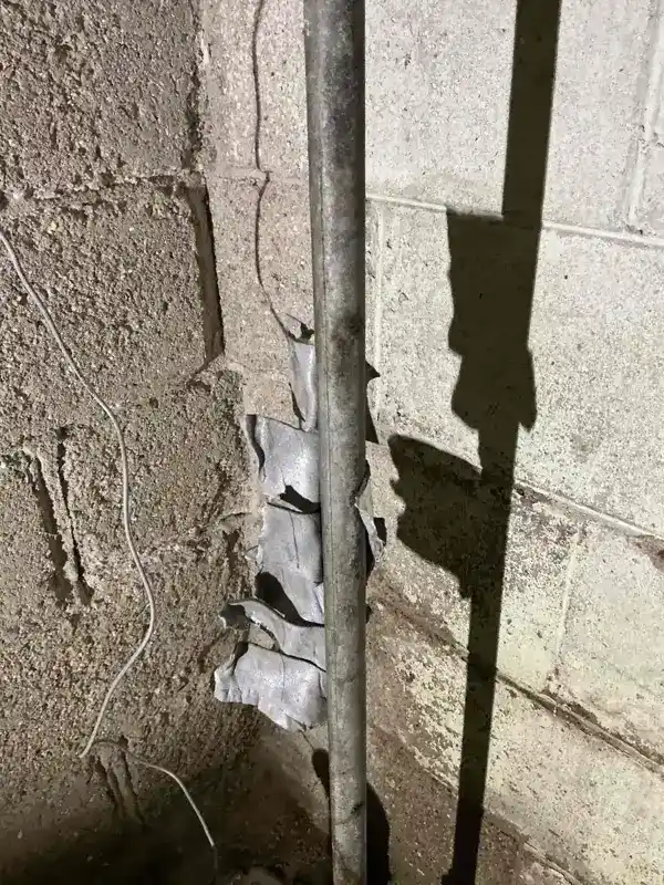 Supply pipe running down a concrete block foundation wall with torn insulation around it