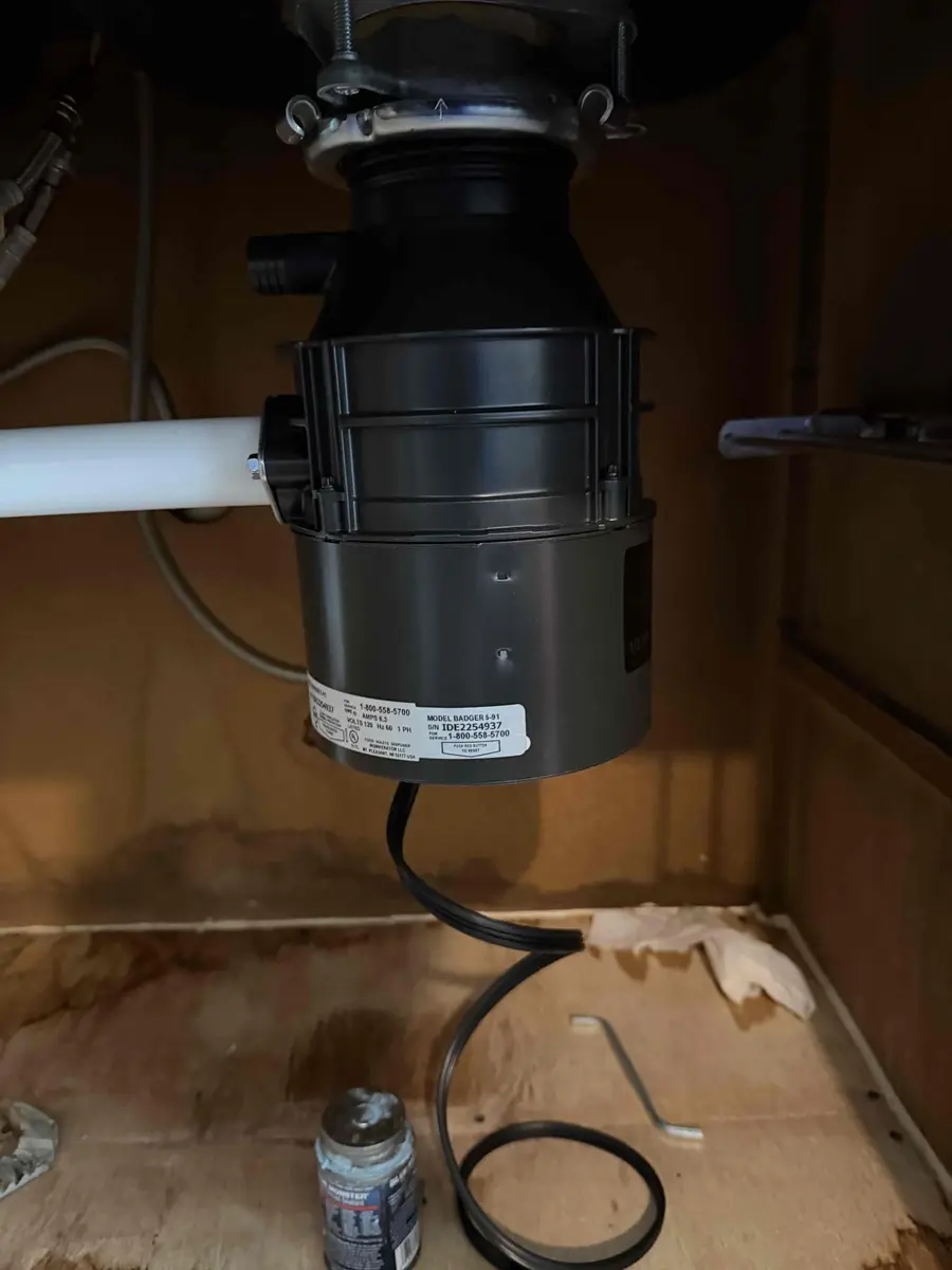 Garbage disposal mounted under a kitchen sink with the outlet pipe and power cord visible