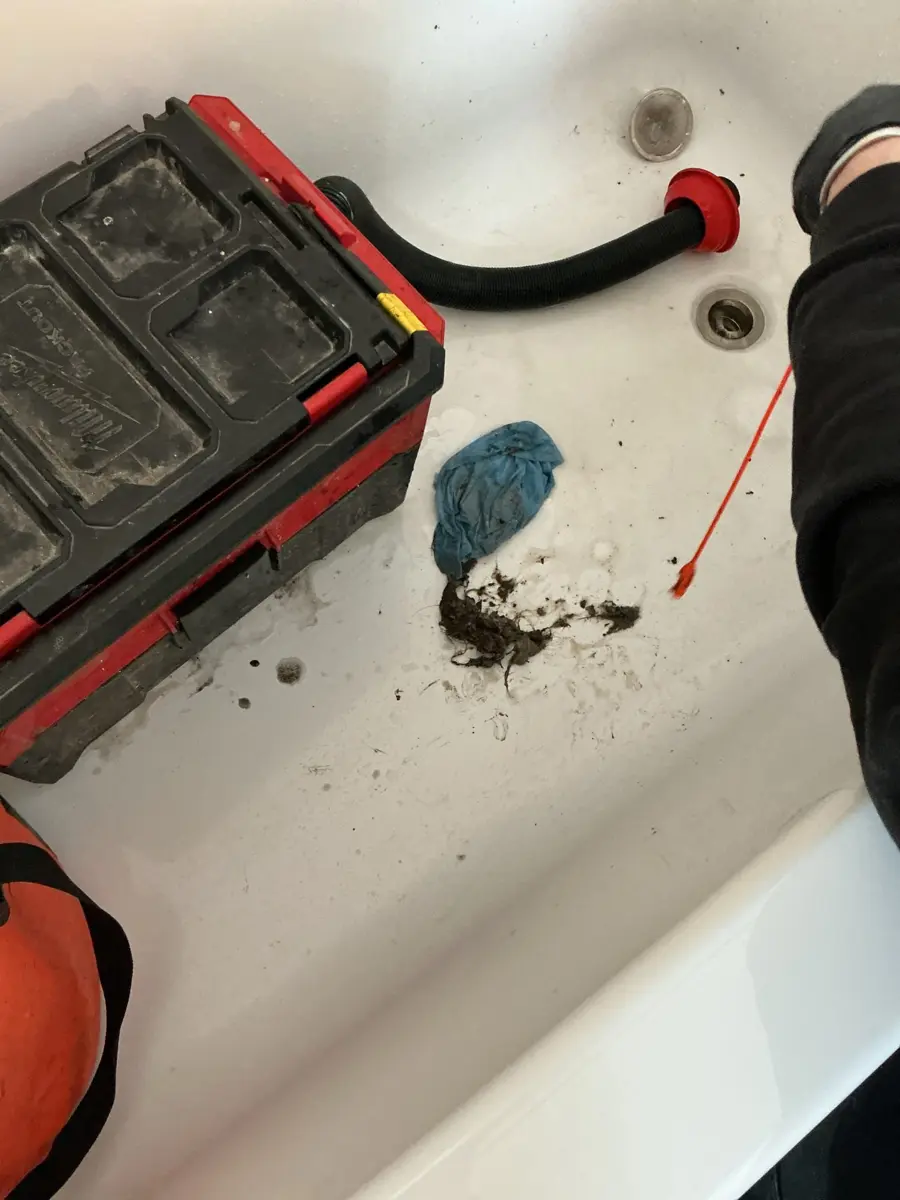 Drum snake beside a bathtub with a pile of hair and sludge pulled from the drain