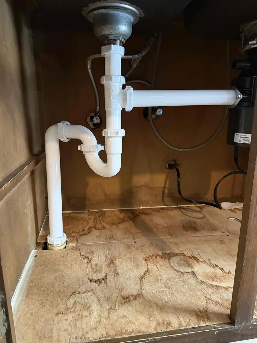 Kitchen sink drain pipes under the counter showing the P trap, the disposal outlet pipe and the drain going into the wall