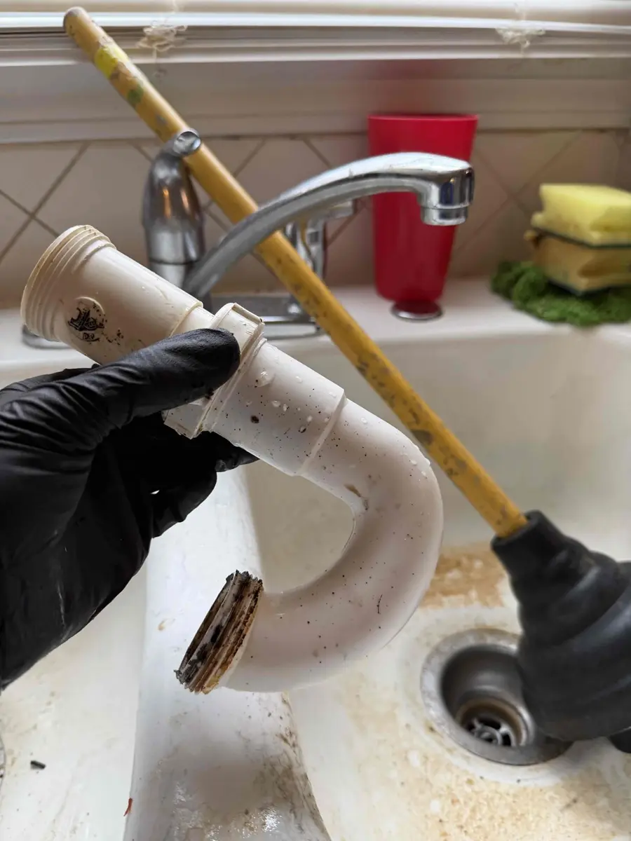 Plumber holding a kitchen sink trap removed to clear a clog