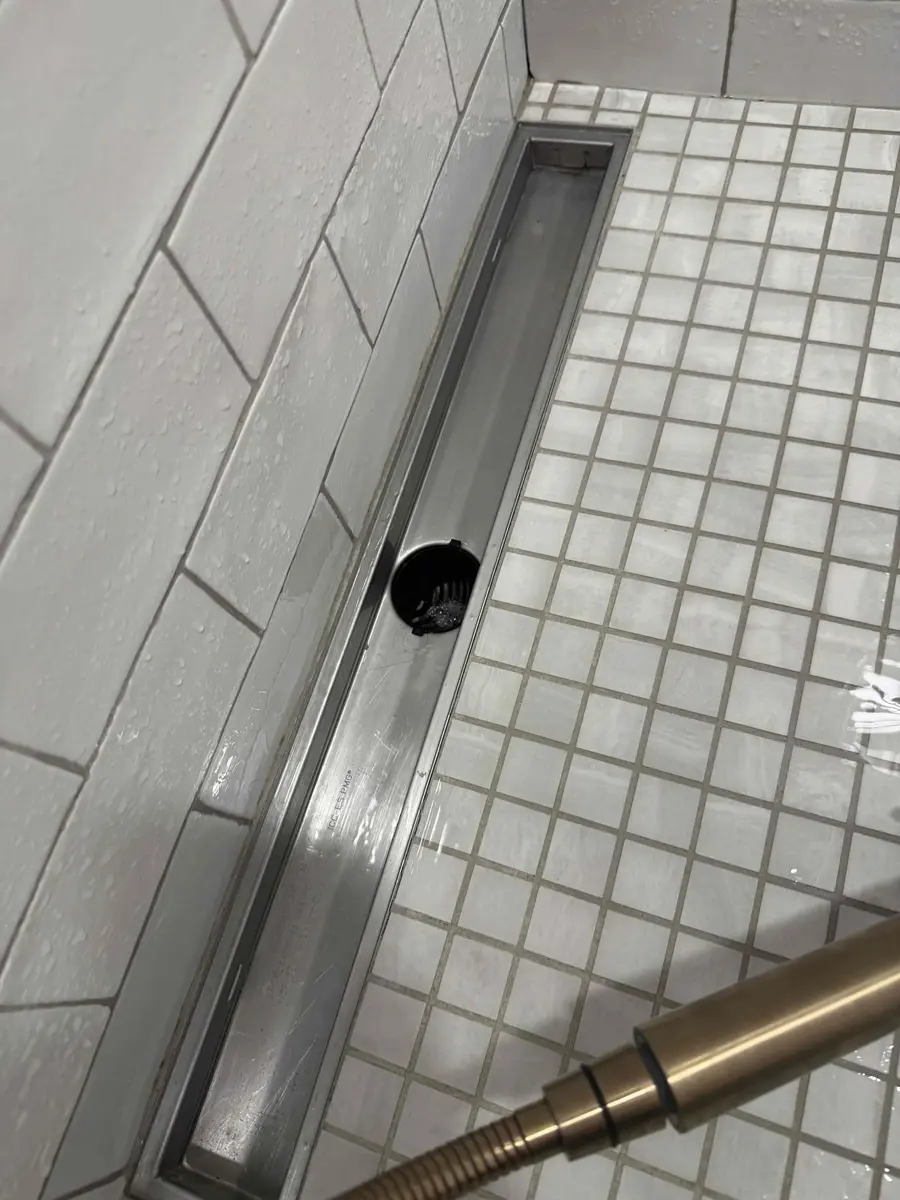 Long stainless linear shower drain with the grate removed showing the drain opening at one end