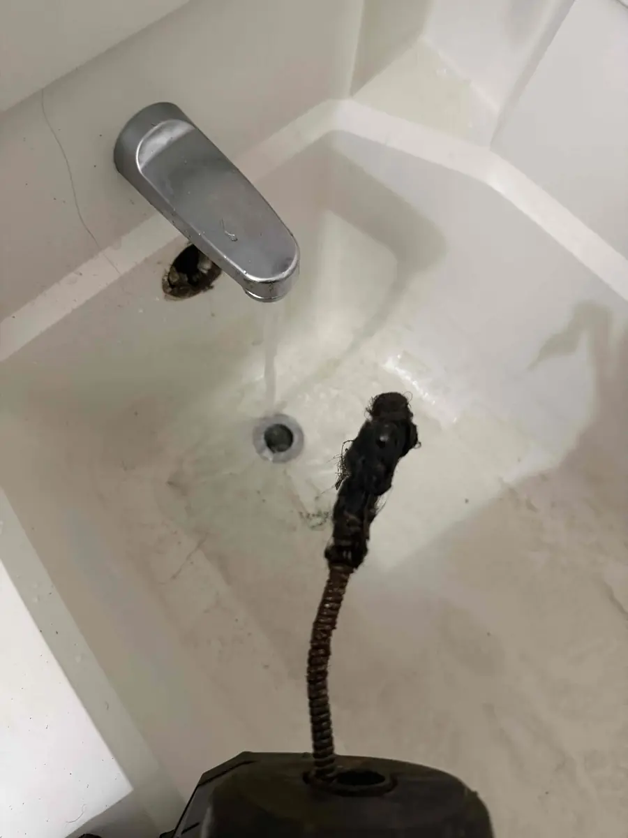 Bathtub with a drum snake cable pulling a long rope of black hair out of the drain