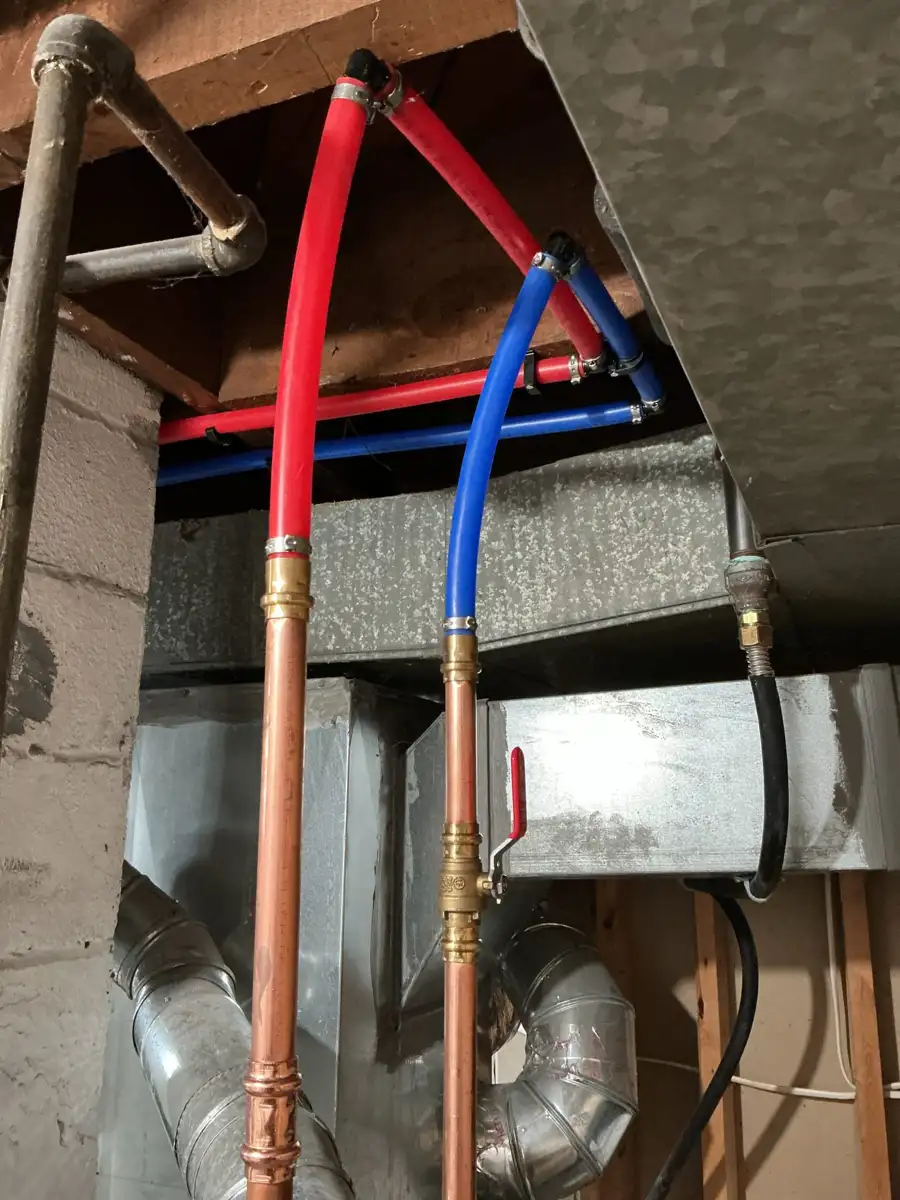 New red and blue PEX water lines replacing old galvanized pipe in a basement