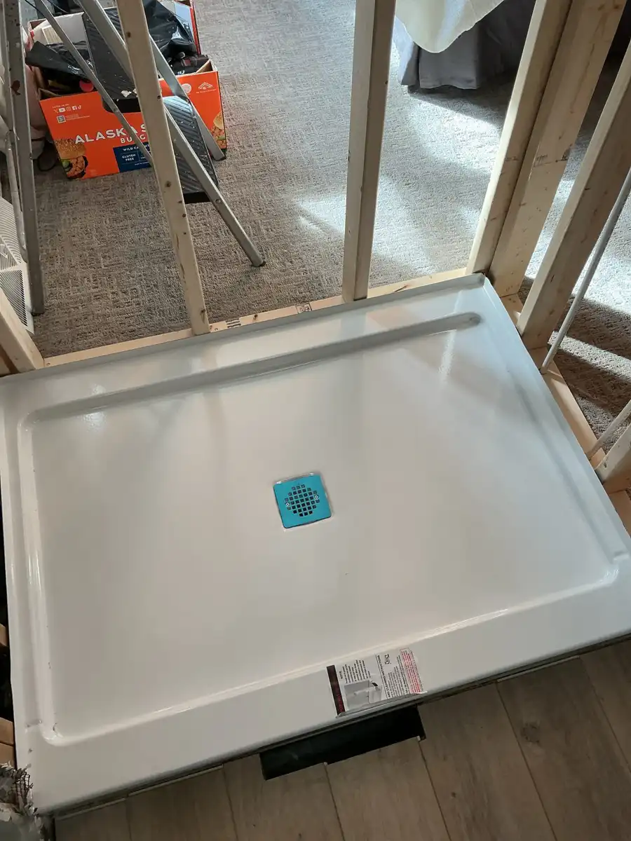 New white shower base set in a framed opening during a bathroom remodel with the drain in place