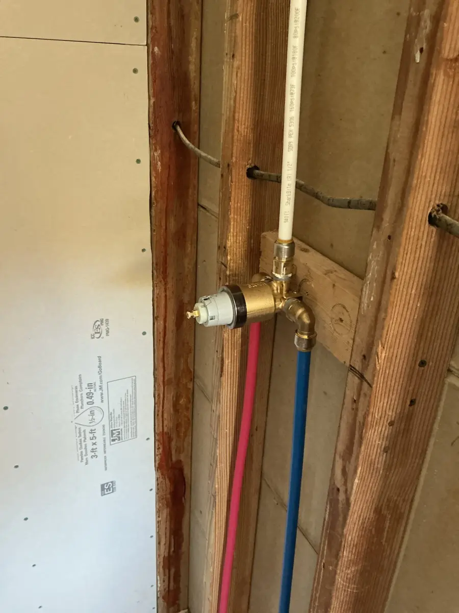 New shower valve installed in an open wall with red and blue supply lines connected