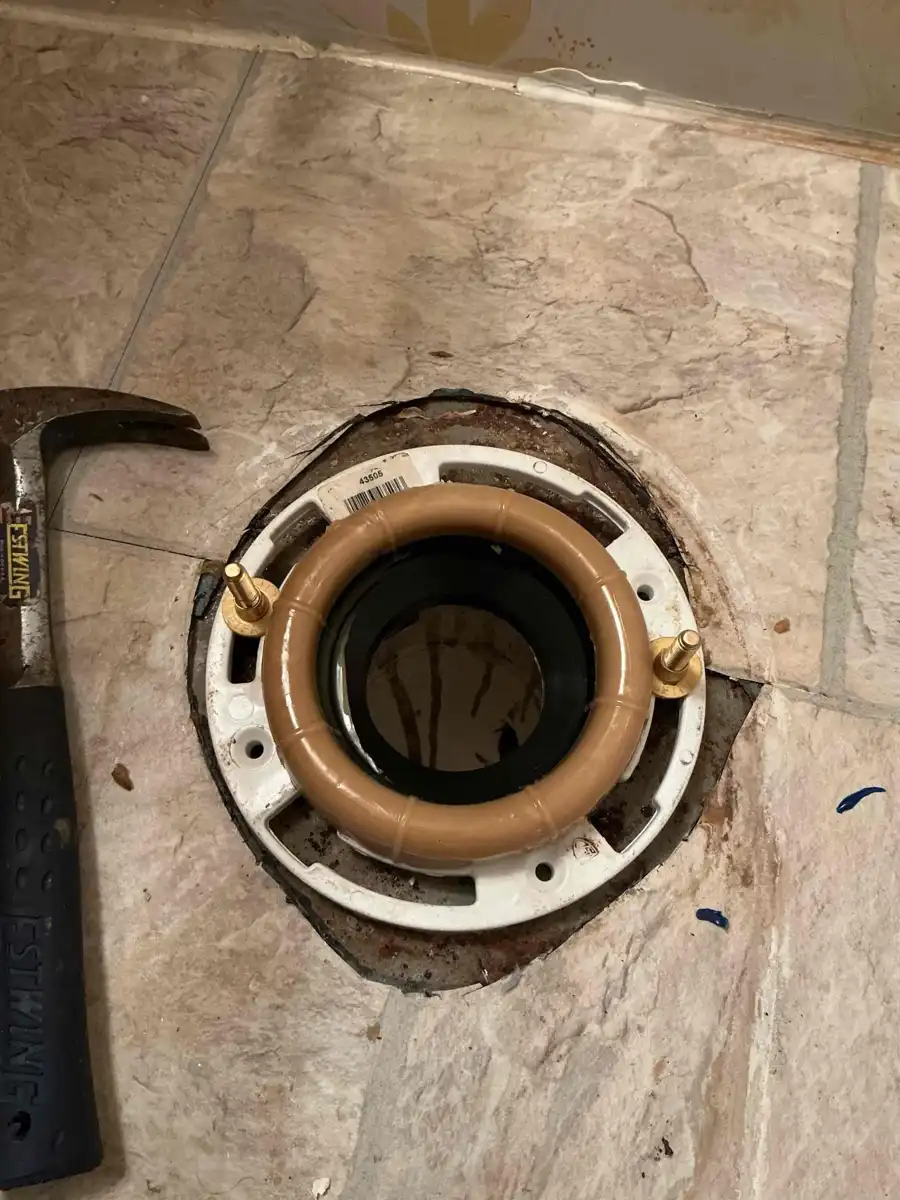 New white toilet flange screwed to the floor with a fresh tan wax ring and brass bolts