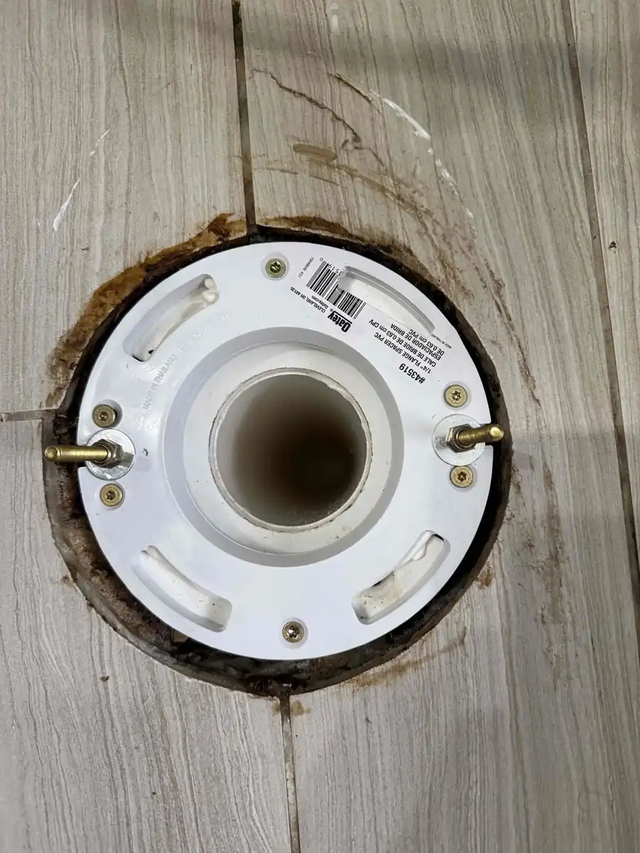 New white toilet flange with brass bolts installed flush in a bathroom floor