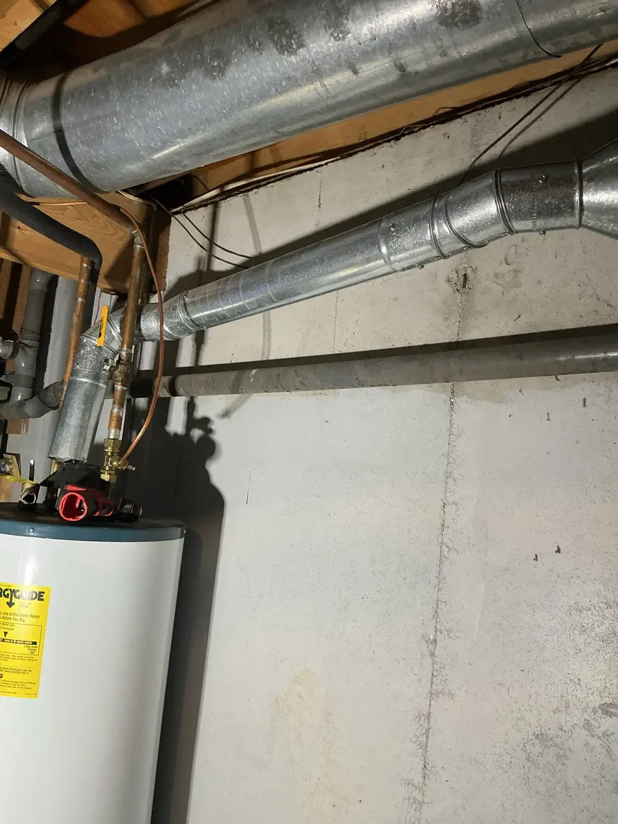 An older gas water heater with visible corrosion and water staining around the base and lower connections