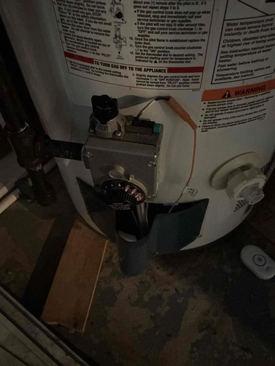 The gas control valve on a water heater showing the thermostat dial set to the Pilot position, with pilot lighting instructions printed on the tank label above it