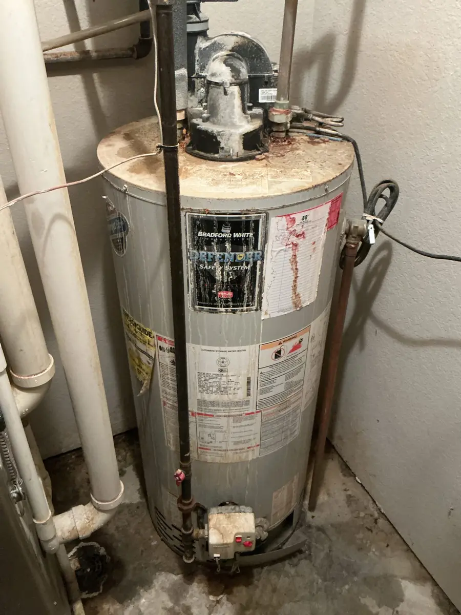 An old Bradford White Defender water heater with heavy corrosion on the top, peeling labels, and rust stains running down the side of the tank
