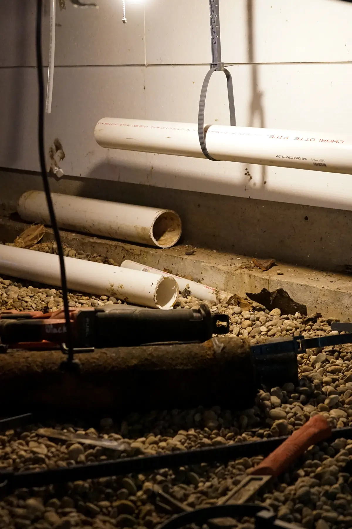 Old rusted cast iron drain pipe removed and lying below new PVC pipe in a crawlspace