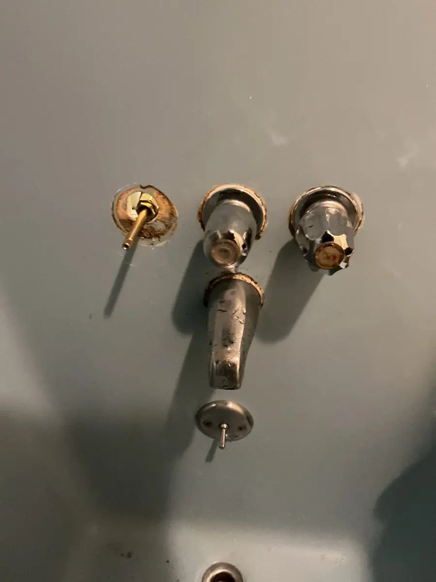 Old three handle shower valve with handles removed and brass stems sticking out of the wall