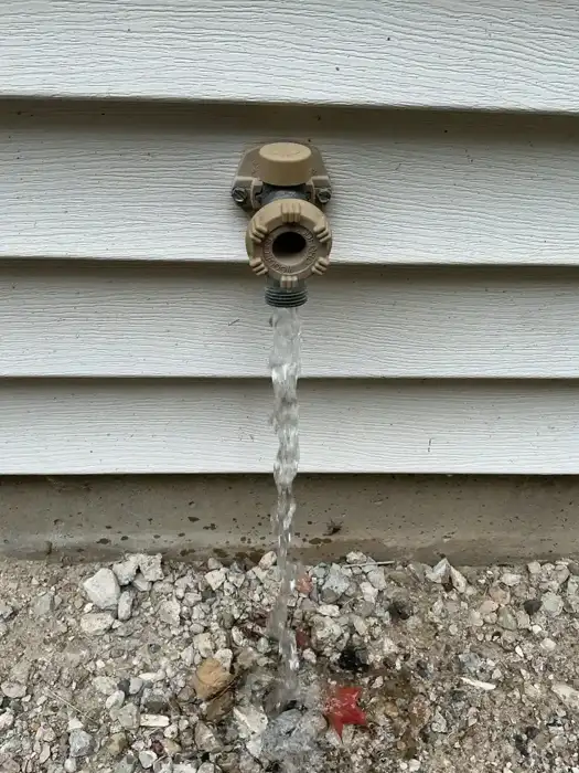 Water flowing out of an outdoor faucet onto gravel as the line drains