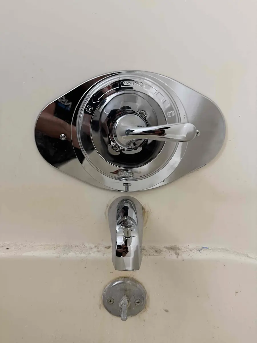 Oval chrome cover plate behind a new single handle shower valve covering the old three handle holes