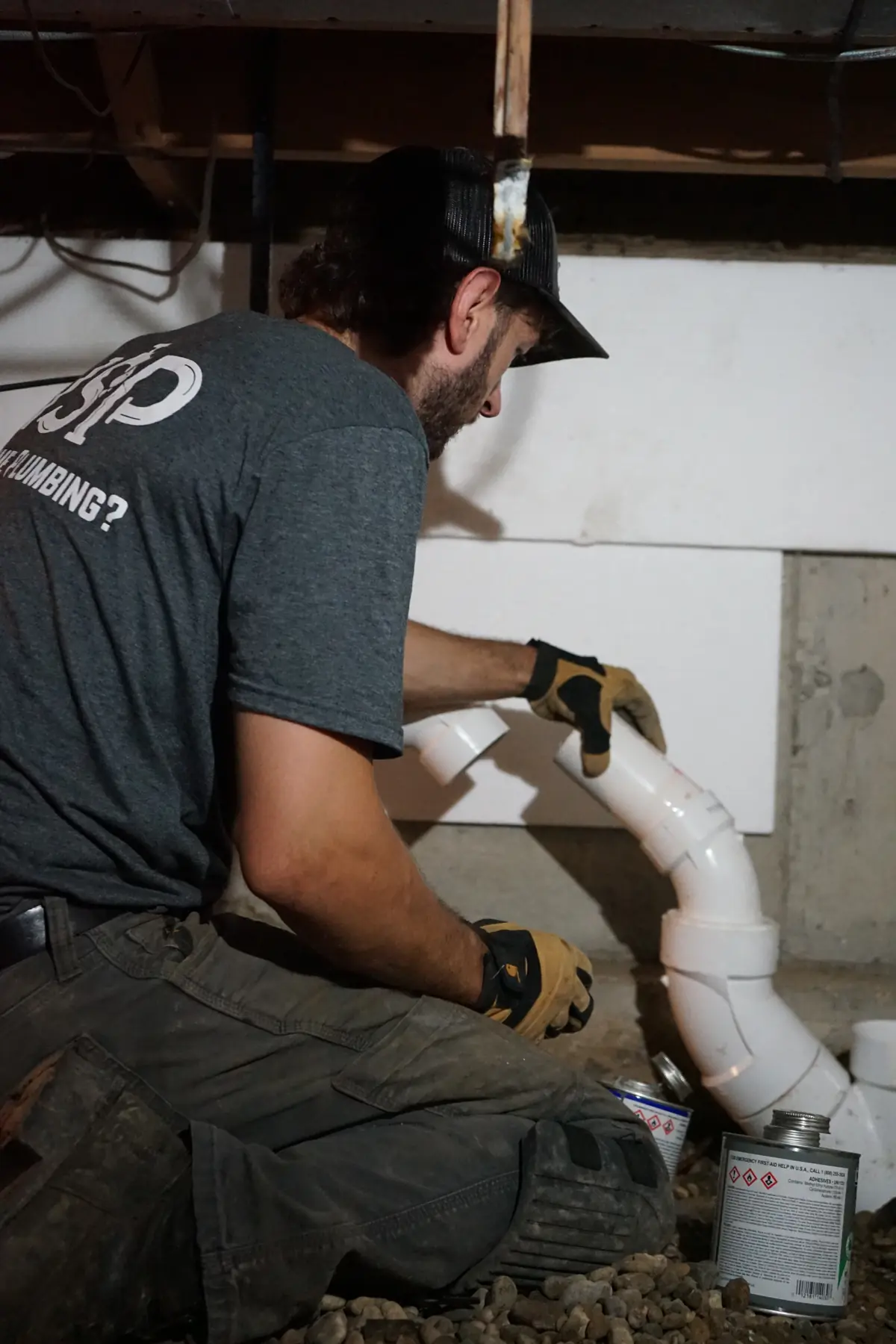 NSP Plumbing plumber gluing a PVC drain fitting in a crawlspace