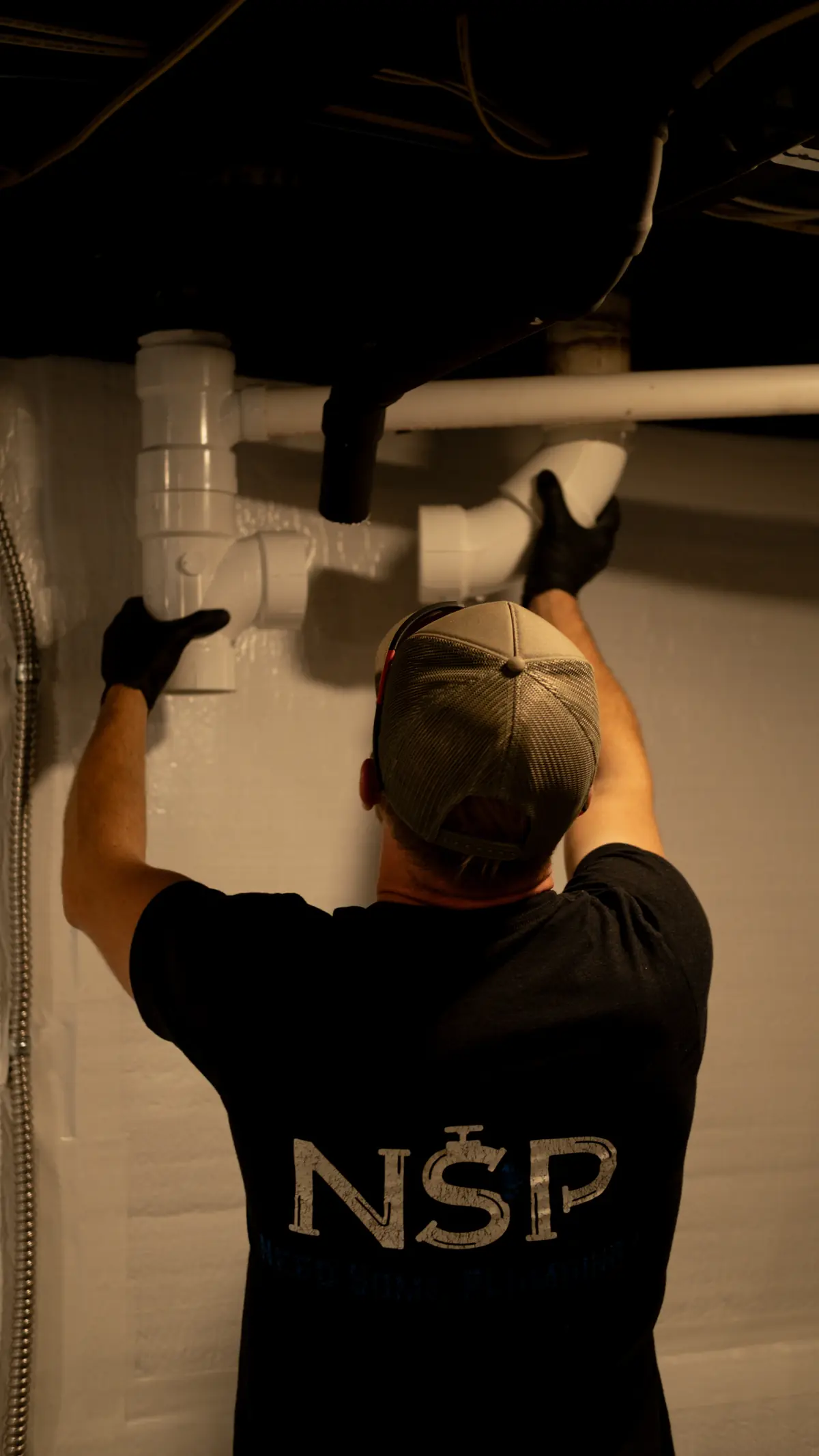 NSP Plumbing plumber installing new PVC fittings on a drain stack in a basement