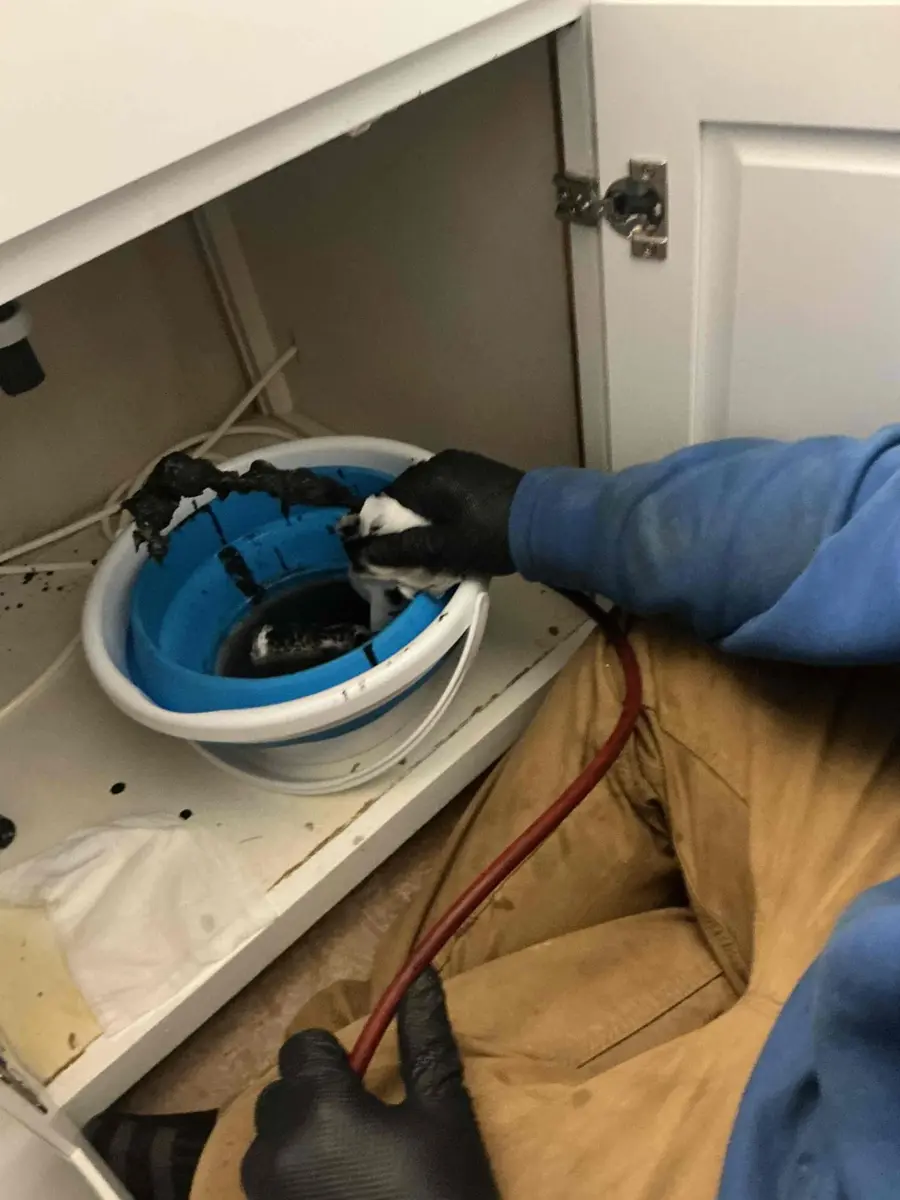 Plumber snaking a slow bathroom sink drain into a bucket after Drano did not work
