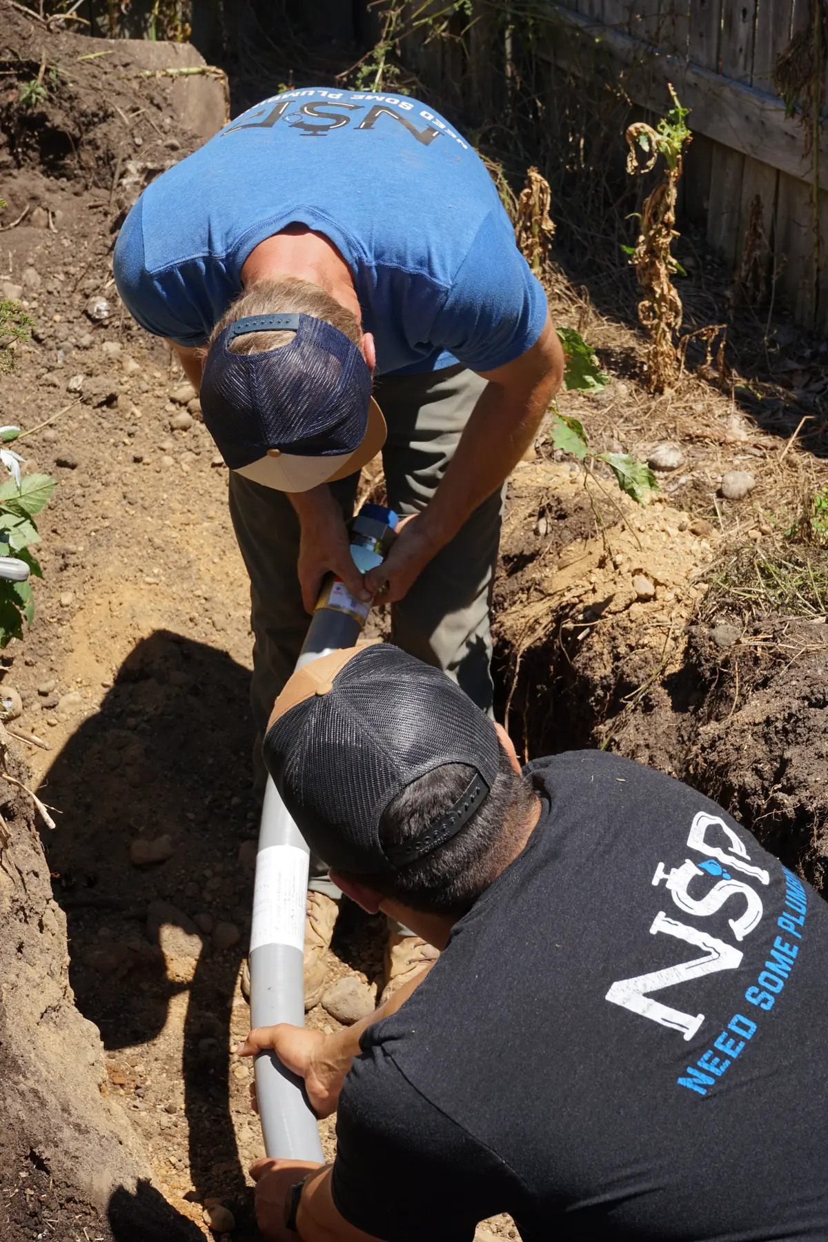 NSP Plumbing plumbers connecting a section of new buried gas line in a backyard trench